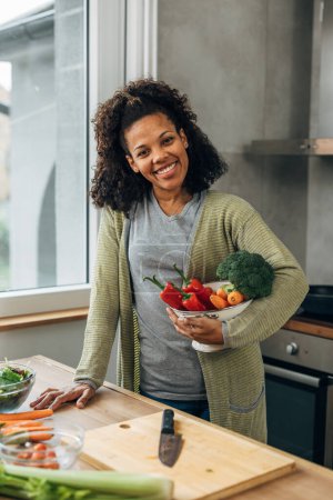 Photo for Portrait of a happy woman holding a bowl of vegetables in the kitchen - Royalty Free Image