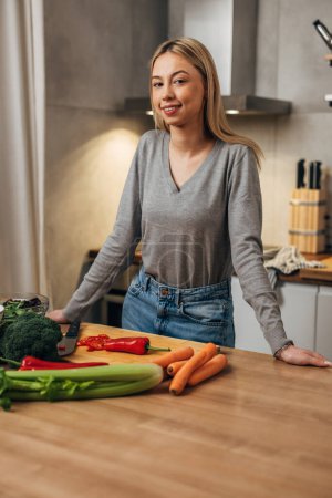 Photo for A young woman is standing in front of a kitchen table and preparing food - Royalty Free Image