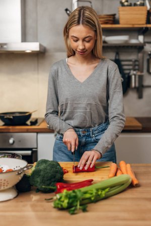 Photo for Front view of a young woman cutting vegetables in the kitchen - Royalty Free Image