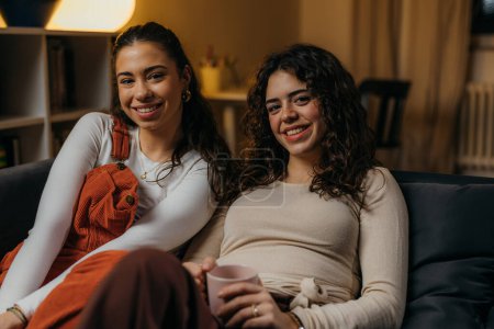 Photo for Two beautiful young women sitting on the sofa together - Royalty Free Image