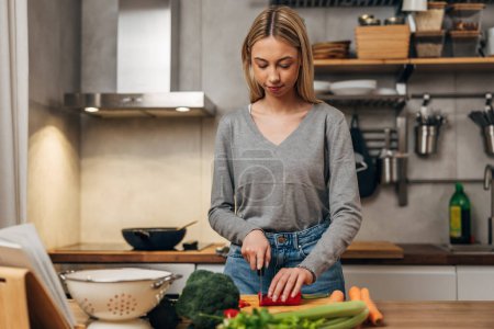 Photo for Front view of a young blonde woman is cutting vegetables - Royalty Free Image
