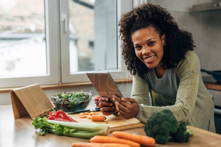 Téléchargez les photos : Une femme souriante s'appuie sur la table avec des légumes dessus et tient la tablette - en image libre de droit