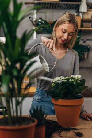 Photo for A blonde woman uses a watering can to water the plants - Royalty Free Image