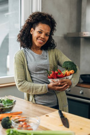 Photo for A beautiful happy woman is holding a bowl of vegetables for a vegan meal - Royalty Free Image