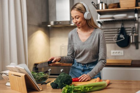 Photo for A young blonde woman is cooking in the kitchen and listening to music - Royalty Free Image