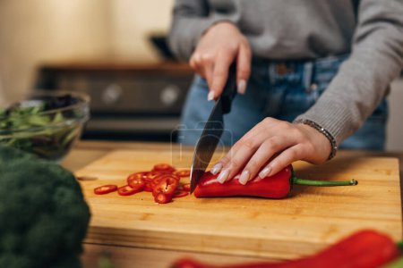 Photo for Closeup view of hands slicing red peeper with a kitchen knife - Royalty Free Image