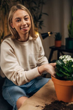 Téléchargez les photos : Une jeune femme regarde la caméra tout en plantant sa plante d'intérieur - en image libre de droit