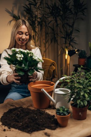 Téléchargez les photos : Une jeune femme met une plante dans un pot de fleurs - en image libre de droit