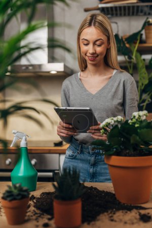 Photo for Woman is surrounded by houseplants and she is using tablet - Royalty Free Image