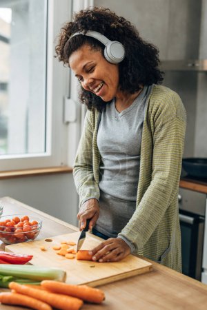 Téléchargez les photos : Gai mixte race femme prépare légumes pour la cuisine - en image libre de droit