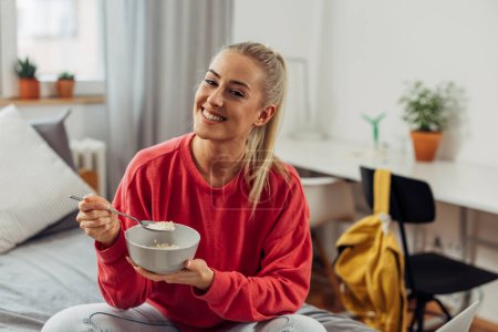 Photo for Happy young woman is eating oatmeal for breakfast - Royalty Free Image