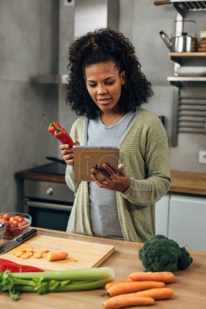 Foto de Una mujer de mediana edad está cocinando en la cocina y sosteniendo una tableta - Imagen libre de derechos