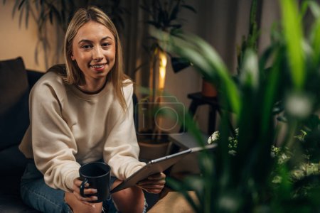 Photo for A young woman surrounded by houseplants in sitting and looking at the camera - Royalty Free Image