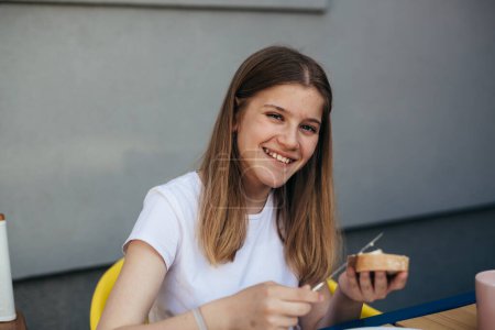 Photo for Happy teenage girl is looking at the camera while spreading butter on the brad for breakfast - Royalty Free Image