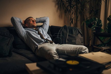 Téléchargez les photos : Un homme écoute de la musique relaxante sur le gramophone après une dure journée de travail - en image libre de droit