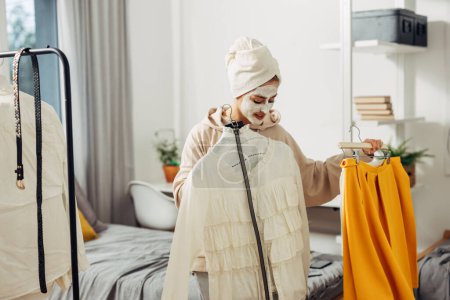 Foto de Una mujer está eligiendo su combinación de ropa mientras espera para quitar la máscara facial - Imagen libre de derechos