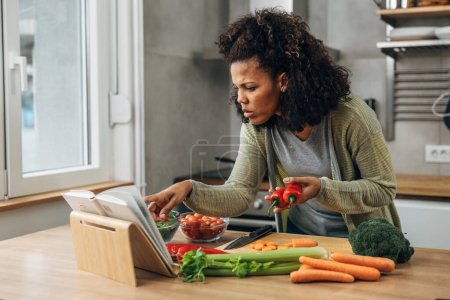 Téléchargez les photos : Une belle femme multiraciale prépare un repas végétalien dans la cuisine en suivant le livre de recettes - en image libre de droit