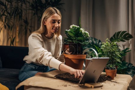Téléchargez les photos : Une fleuriste femme prend une photo d'elle avec une plante à la main en utilisant une tablette - en image libre de droit