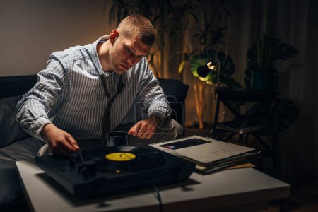 Photo for Tired businessman is playing records on phonograph at home in the evening - Royalty Free Image
