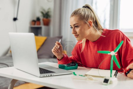 Photo for A beautiful caucasian student, intensely focused on her laptop, doing project on green energy - Royalty Free Image