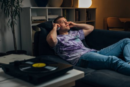Photo for A Caucasian man puts on headphones to listen to records and relax at night - Royalty Free Image