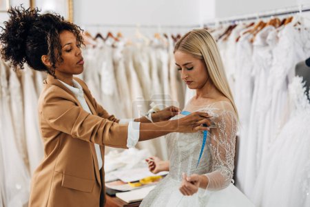 Téléchargez les photos : Une femme tailleur veille à ce que la robe s'adapte parfaitement sur la mariée - en image libre de droit