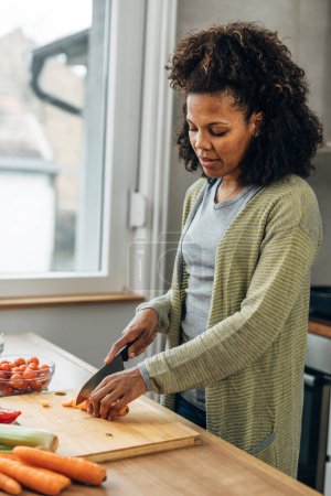 Foto de Mujer afroamericana está cortando zanahorias en la cocina. Preparación de la comida. - Imagen libre de derechos
