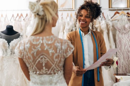 Foto de Sastre multirracial habla con un cliente en un vestido de novia. - Imagen libre de derechos