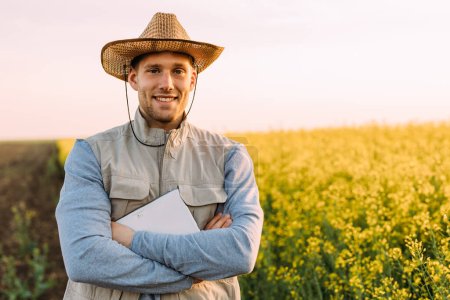 Téléchargez les photos : Vue de face d'un beau fermier caucasien debout sur une terre agricole et regardant la caméra. - en image libre de droit