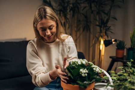Photo for A cute blond woman is potting a plant with white flowers. - Royalty Free Image