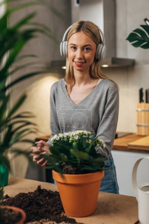 Téléchargez les photos : Portrait d'une jeune femme blonde avec écouteurs empotant une plante. - en image libre de droit