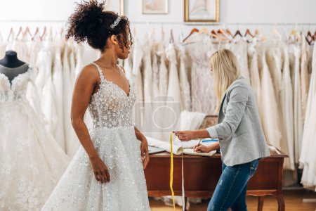 Téléchargez les photos : Un brie multiracial dans une robe de mariée se tient dans un salon de mariée. - en image libre de droit