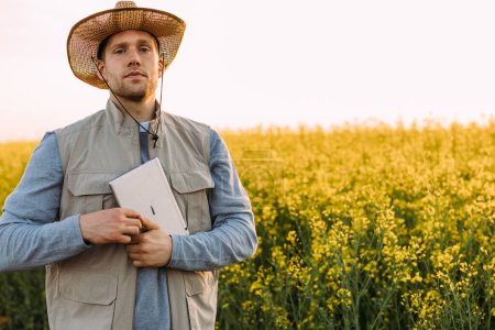 Téléchargez les photos : Vue de face d'un agriculteur caucasien debout dans le champ avec une tablette dans les mains. - en image libre de droit