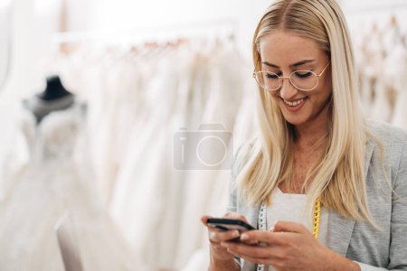 Photo for Closeup view of a Caucasian woman working in a tailoring salon and using her mobile phone. - Royalty Free Image