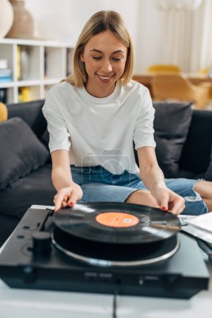 Photo for A pretty blond woman plays vinyl records at home. - Royalty Free Image