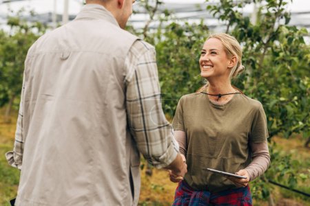 A smiling woman shakes hands with a man in the orchard.