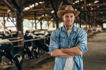 Porträt eines glücklichen Bauern, der in einem Stall voller Kühe steht.