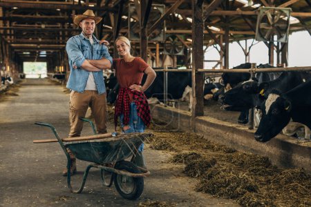 Foto de Vista frontal de un hombre y una mujer de pie en un establo con vacas. - Imagen libre de derechos