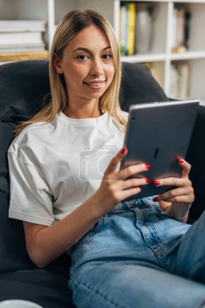 Téléchargez les photos : Une femme blonde utilisant un appareil tablette à la maison. - en image libre de droit