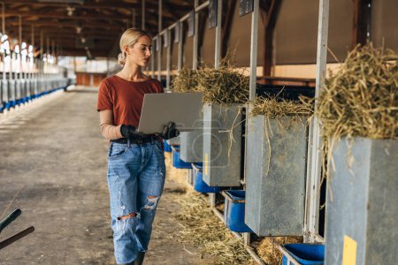 Photo for Modern female farmer using laptop in a stable. - Royalty Free Image
