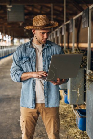 Foto de Vista frontal de un hombre con un portátil de pie en una granja de animales grandes. - Imagen libre de derechos