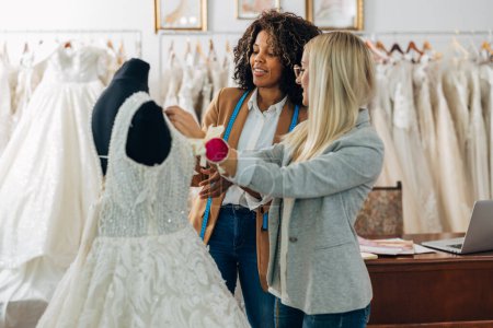 Téléchargez les photos : Deux femmes travaillent ensemble sur une nouvelle robe de mariée. - en image libre de droit