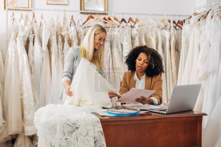 Téléchargez les photos : Tailleur et designer travaillent ensemble sur la création de robes de mariée dans un salon de mariée. - en image libre de droit