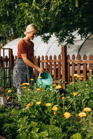 Téléchargez les photos : Belle femme heureuse prenant soin de ses fleurs dans le jardin. - en image libre de droit
