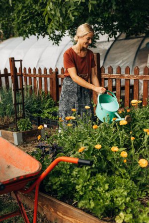 Téléchargez les photos : Heureux jardinier femelle arrose les plantes dans le jardin. - en image libre de droit