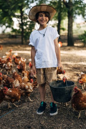 Foto de Vista frontal de un lindo chico caucásico en una granja de pollos alimentando a los pollos. - Imagen libre de derechos