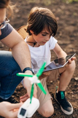 Foto de Primer plano de un niño jugando con un molino de viento y una tableta con su padre. - Imagen libre de derechos