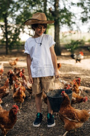 Foto de Feliz chico caucásico alimentando pollos al aire libre. - Imagen libre de derechos