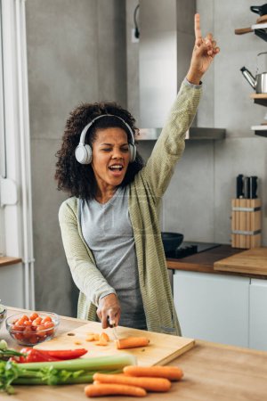 Photo for Cheerful woman is enjoying cooking while listening to music. - Royalty Free Image