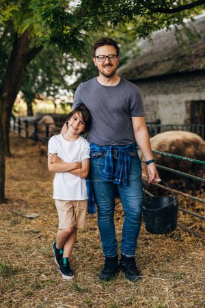 Téléchargez les photos : Vue de face d'un garçon debout à côté de son père à la ferme animalière. - en image libre de droit